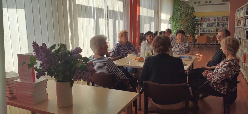 Zdjęcie kolorowe, uczestniczki Dyskusyjnego Klubu Książki na spotkaniu w Bibliotece siedzą przy stole i rozmawiają