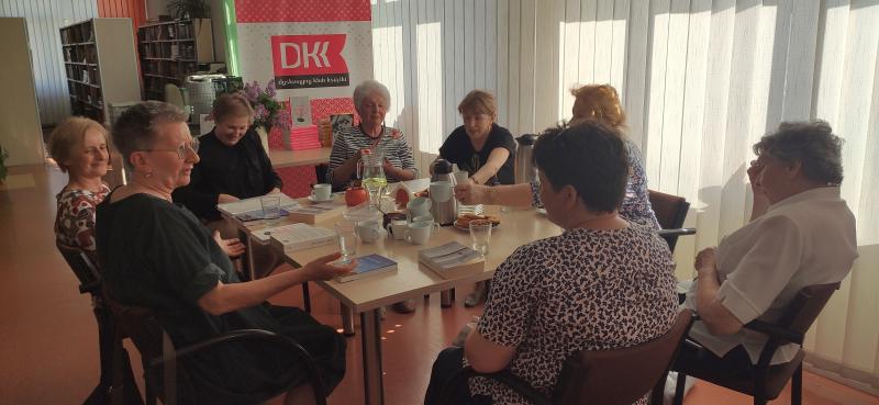 Zdjęcie kolorowe, uczestniczki Dyskusyjnego Klubu Książki na spotkaniu w Bibliotece siedzą przy stole i rozmawiają