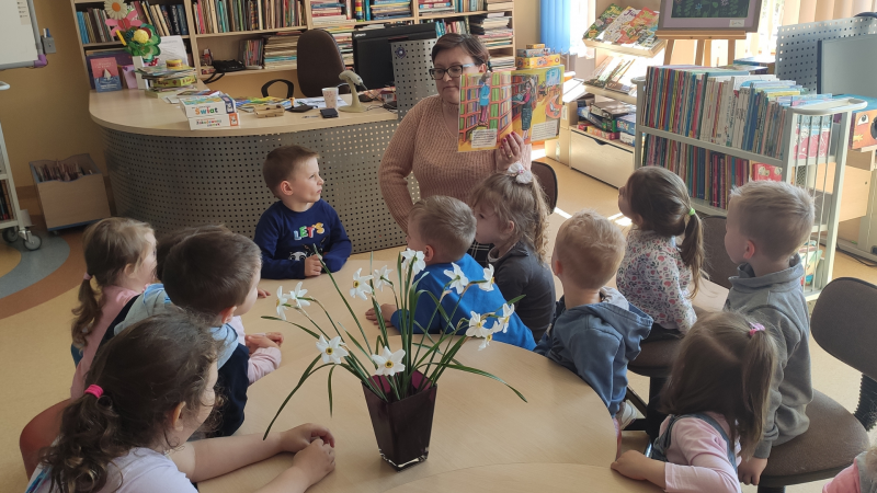Zdjęcie kolorowe, przedszkolaki z życzeniami z okazji dnia bibliotekarza w bibliotece