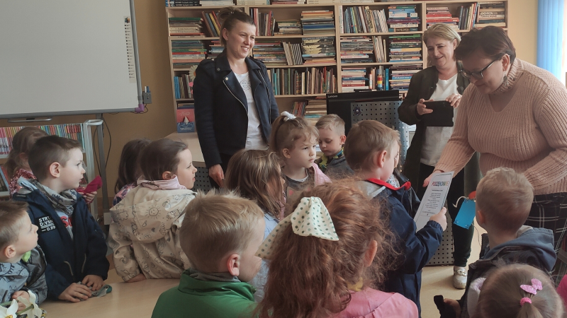 Zdjęcie kolorowe, przedszkolaki z życzeniami z okazji dnia bibliotekarza w bibliotece